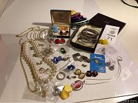 Full assortment of vintage jewelry including necklaces, bracelets, earrings, pins on a white surface