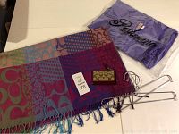 Photo showing a colorful Coach scarf, a purple Pashmina scarf in original packaging, and a Coach cardholder with monogram pattern, along with metal hangers.