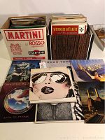 Photo showing two boxes filled with assorted vinyl records with several record sleeves laid out in front. Visible covers include The Steve Miller Band 'Book of Dreams', an album cover featuring a person wearing sunglasses, and other classic rock and orchestral album art.