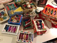 Photo of various vintage glass Christmas ornaments in original boxes and loose figurines on a table.