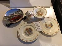 Photo showing four Bunnykins china dish pieces: two plates, one bowl, one mug, all decorated with rabbit illustrations and bunny border pattern.