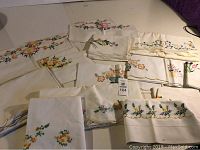 Overhead view of various embroidered linens including sheets and pillowcases with floral embroidery in multiple colors (yellow, orange, pink, green).
