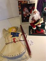 Photo of vintage Santa figurine with cassette player and light-up angel with attached wiring, placed on a flat surface.