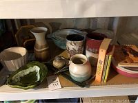 Shelf with vintage ceramic and glass kitchenware, including bowls, vases, casserole dishes, and vintage cookbooks.