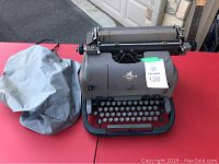 Underwood manual typewriter set on a red surface with grey protective fabric cover next to it.