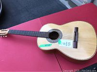 Full view of classical acoustic guitar on red surface showing natural wood finish and 39 inch height indicated on tape.
