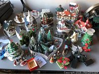 Overview of multiple ceramic village buildings, snow-covered trees, figurines, and decorations on a table