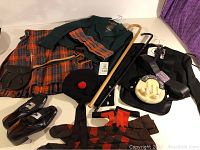 Photo showing full lot with Scottish tartan kilt, green jacket, black sporran with fur front, Glengarry cap, socks, belts, shoes and walking sticks