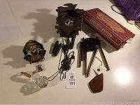 Photo showing two cuckoo clocks (one larger wooden with pine cone weights, one smaller colorful), wooden wind chimes, and boxed items on table.