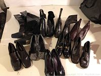 Photo showing the full lot of 11 pairs of women's shoes and boots in size 10 laid out on a table, mostly black and brown styles.