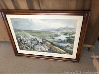Framed lithograph leaning against wall showing a scenic train and settlement landscape