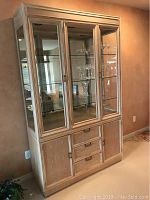 Front view of Drexel Heritage mid-century modern china hutch showing wood grain, glass doors, and shelves with some crystal glasses inside.