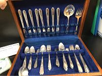 Full view of the silverplate flatware arranged in the original wooden box lined with blue velvet showing most items secured by fabric loops.