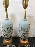 Front view of both lamps showing light blue porcelain bodies with gold botanical design on square gold-tone bases