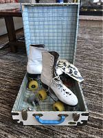 Photo of vintage white leather women's roller skates inside open vintage dented metal carrying case with blue handle and plaid interior lining.