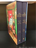 Two hardcover books in dark fabric with gold lettering on spine housed in illustrated slipcase.