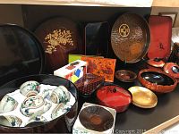 Wide view of multiple vintage Japanese lacquer items including the large round lacquer box holding tea pot and six teacups, lacquer trays, bowls, and boxes