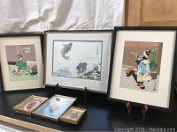 Overall arranged display of three Japanese prints in wood frames, two small dried flower frames, all on a surface with a plastic bin visible.