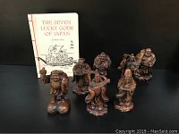 Photo of all seven ceramic Lucky Gods figures arranged in a row with the book 'The Seven Lucky Gods of Japan' behind them.