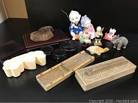 View of entire lot showing ceramic boy and girl figurines, animal figurines including cat and elephant, wooden templates, black round stands, and white plastic mold.