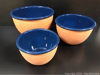 Three vintage nesting bowls, smallest, medium and largest are peach on the outside and blue on the inside, placed on a dark background.