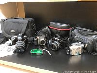 Photo showing the full lot including various cameras, camcorder and camera bags displayed on a table.