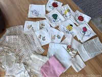 Multiple vintage stitched and printed flour sack tea towels, crocheted linens, table cloth with matching napkins spread out on floor.