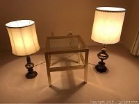 Photo of the two brass lamps with fabric lampshades and the brass and glass end table between them