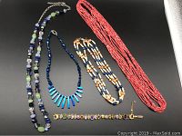 Full view of the four necklaces and one charm bracelet laid flat on a black surface showing color and size variation