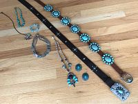 Full view of all items including two leather belts with turquoise-colored conchos and multiple pieces of turquoise-themed jewelry including necklaces, bracelet, and earrings laid out on wooden surface.