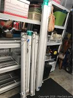Six rolled-up white outdoor sun shades standing upright near shelving in garage or storage area.