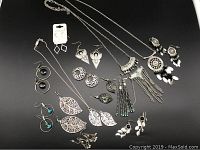 Full view of all 15 pieces showing assortment of silvertone earrings, necklaces with leaf motifs, beads, and geometric shapes.