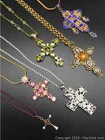 Set of six cross pendants and necklaces displayed on black background showing size, style, and color variety