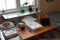 Overview of items on a glass desk, including the brown leather blotter, green desk lamp, pencil sharpener, letter holders, waste basket, paper shredder, and package of office paper.