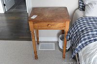 Front view of small wooden nightstand table beside bed, showing top surface and drawer with knob