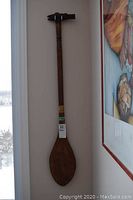 Full length photo of the wooden paddle hanging on the wall showing its size and shape.