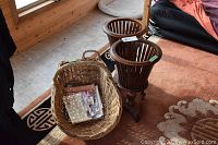 Overall view of the large wicker basket filled partially with magazines and two wooden fern stands on a carpet.
