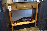 Shark handheld vacuum in purple and black color with charger cable laid on open lower shelf of side table, vacuum labeled as untested.