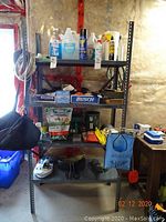 Full view of metal shelving unit with various cleaning products, garden supplies, car care items, boots, and miscellaneous household items.