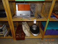 Photo of shelves showing vintage Health Meter scale on bottom shelf with leather case and cloth bag, Ikea shelving unit parts on middle shelf, and purple storage bins on right side.