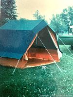 Blue and orange 4 man Legionowo barn style tent setup on grass with poles and guy lines visible.