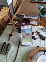 Schneider cuckoo clock parts including carved leaves, pine cone weights, and a VHS tape on a table