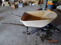 Full side angle view of the fiberglass wheelbarrow showing wood handles, fiberglass tub, black pneumatic tire and metal frame with some rust.
