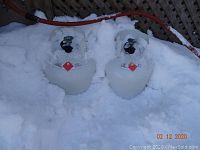 Two white propane tanks with 20lb capacity, red flammable warning labels, and valves with protective covers, placed outdoors in the snow.