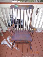 Wooden painted rocking chair with vertical spindles and curved top rail, showing peeling paint and wear, placed on a porch deck with snow visible on the floor.