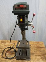 Front view of the Sears Craftsman 8 inch drill press on wood surface, showing base, column, table, and head with cord coiled beside it.