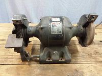 Front view of the Thor bench grinder showing the heavy cast iron base and motor section with grinding wheel on one side and wire brush on the other.