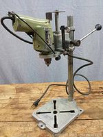 Manual drill press front view showing drill mounted on aluminum post and base with lever for spindle movement.