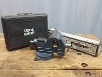 Blue bench vise with case and other boxed tools behind on wood table
