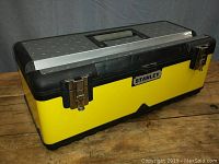 Closed view of the yellow and black Stanley metal tool box with stainless steel deck on top, two metal latches and handle